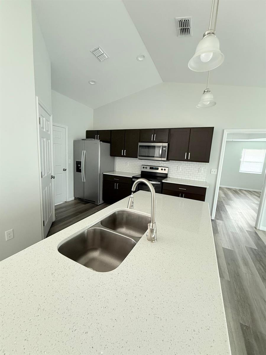 A kitchen with dark cabinets, stainless steel appliances, and a large white quartz island — 6823 SW 129th Street, Ocala FL 34473, OCALA, FL