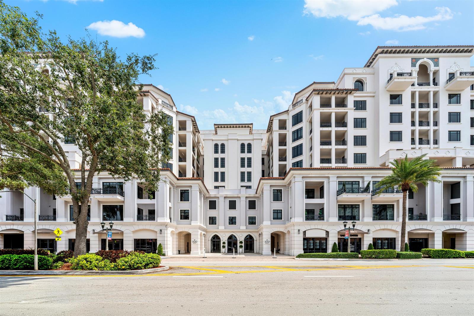 A multi-story white building with arched entrances and balconies stands behind a paved street — 200 E Palmetto Park Road # 404, Boca Raton FL 33432, BOCA RATON, FL
