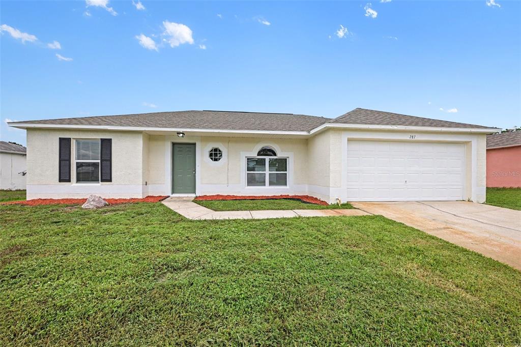 A single-story house with a green front door, white garage, and a grassy front yard — 287 DELAKE ROAD NW, PALM BAY, FL