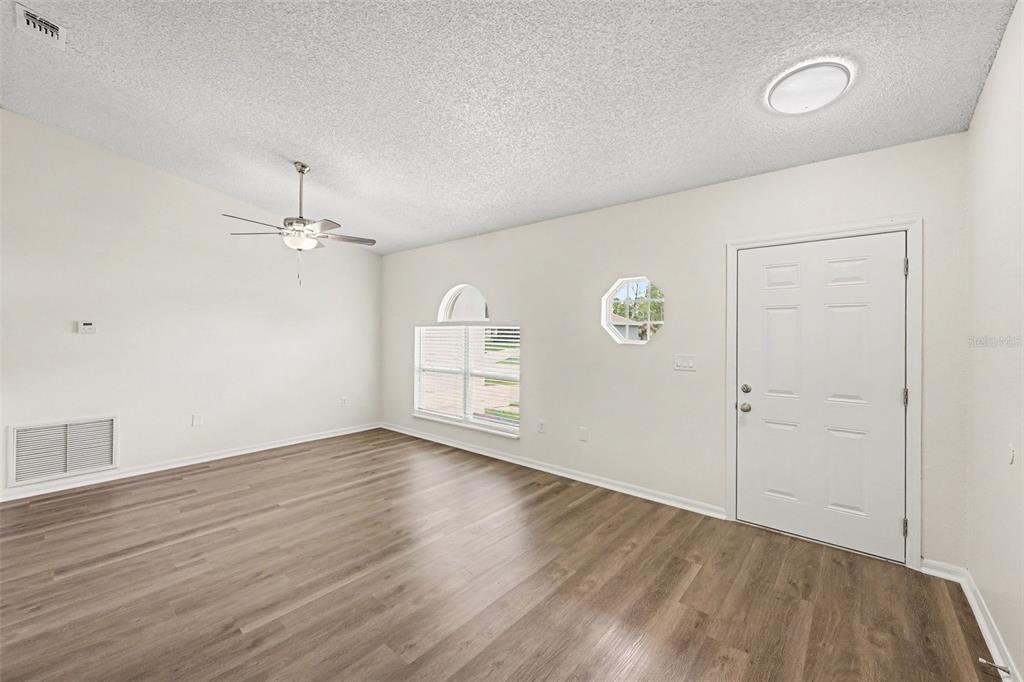 An empty room features wood-look flooring, a ceiling fan, a window, and a white door — 287 DELAKE ROAD NW, PALM BAY, FL