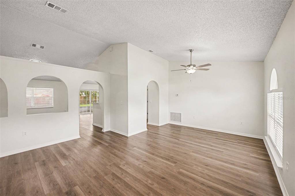An empty living room features wood-look flooring, white walls, arched doorways, and a ceiling fan — 287 DELAKE ROAD NW, PALM BAY, FL