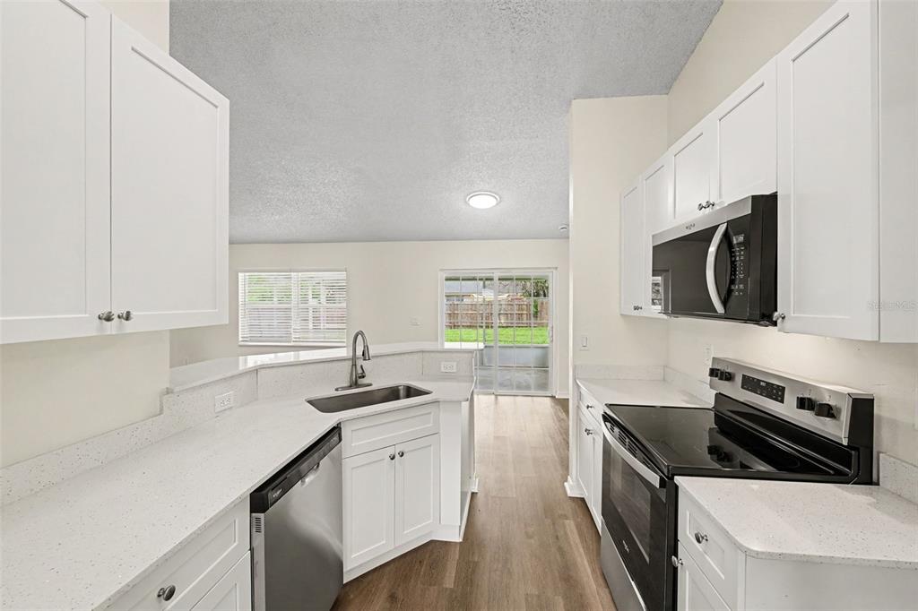 A kitchen with white cabinets, stainless steel appliances, and quartz countertops overlooks a living area — 287 DELAKE ROAD NW, PALM BAY, FL