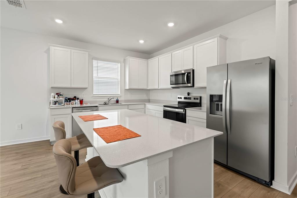 A modern kitchen features white cabinets, a large quartz island, and stainless steel appliances — 11226 SYCAMORE GLEN LOOP, THONOTOSASSA, FL