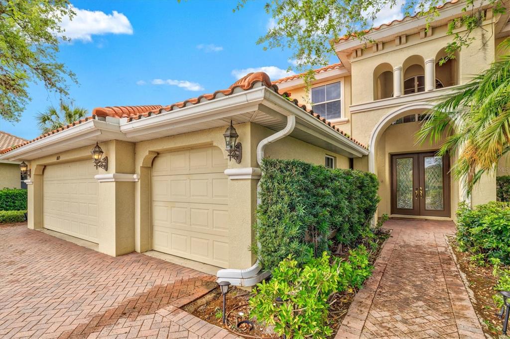 A two-car garage and arched entryway of a stucco home with a tiled roof — 10115 DAY LILY COURT, BRADENTON, FL