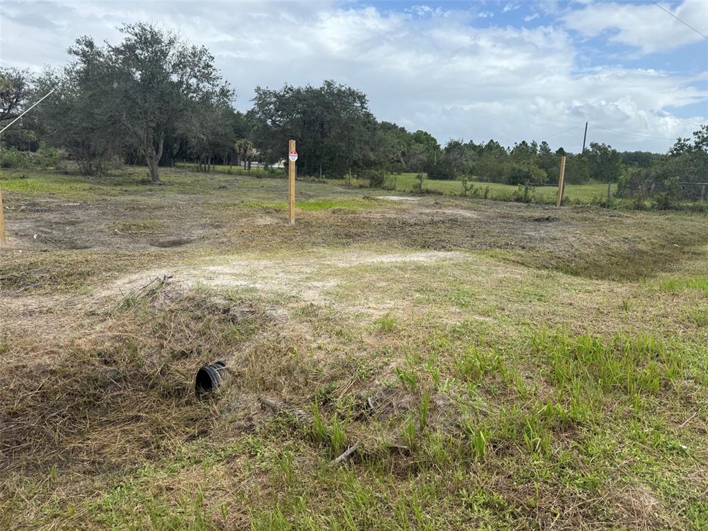 A vacant, grassy lot features a drainage culvert and several wooden survey stakes — 15723 NW 304TH STREET, OKEECHOBEE, FL