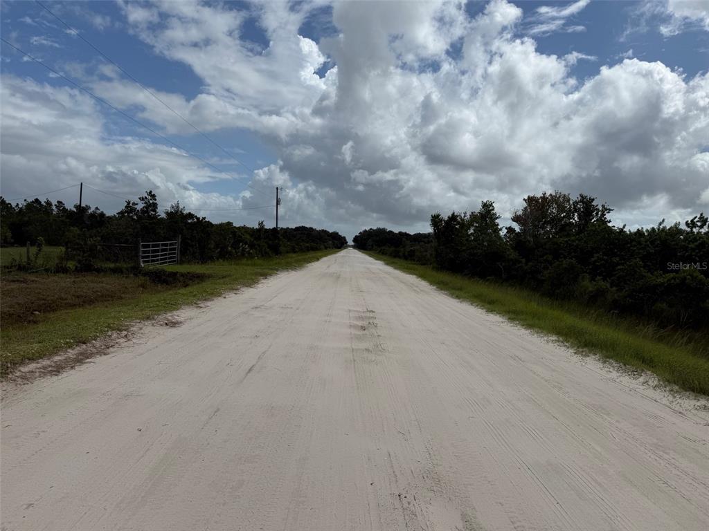 A long, straight dirt road stretches through a rural landscape under a cloudy sky — 15723 NW 304TH STREET, OKEECHOBEE, FL