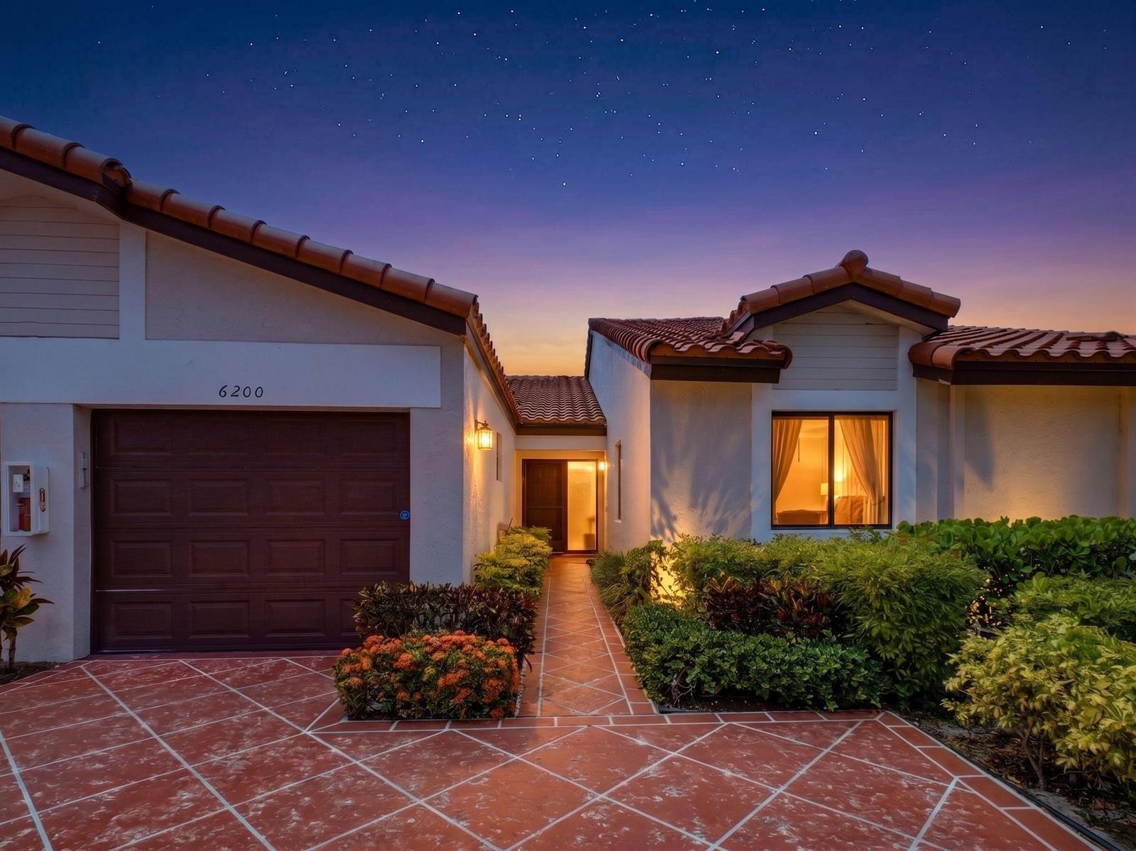 A single-story house with a tiled roof, garage, and walkway at dusk — 6200 Kings Gate Circle, Delray Beach FL 33484, DELRAY BEACH, FL