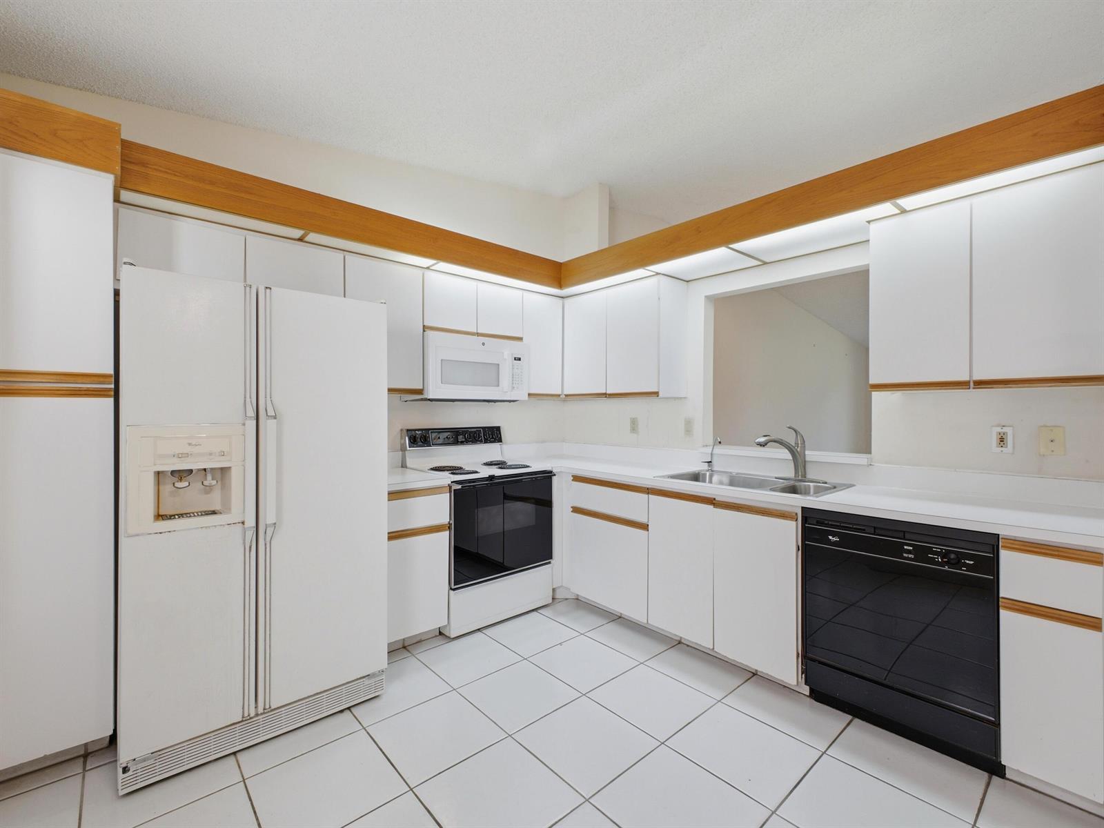 A kitchen features white cabinets with wood trim, white appliances, and white tile flooring — 6200 Kings Gate Circle, Delray Beach FL 33484, DELRAY BEACH, FL