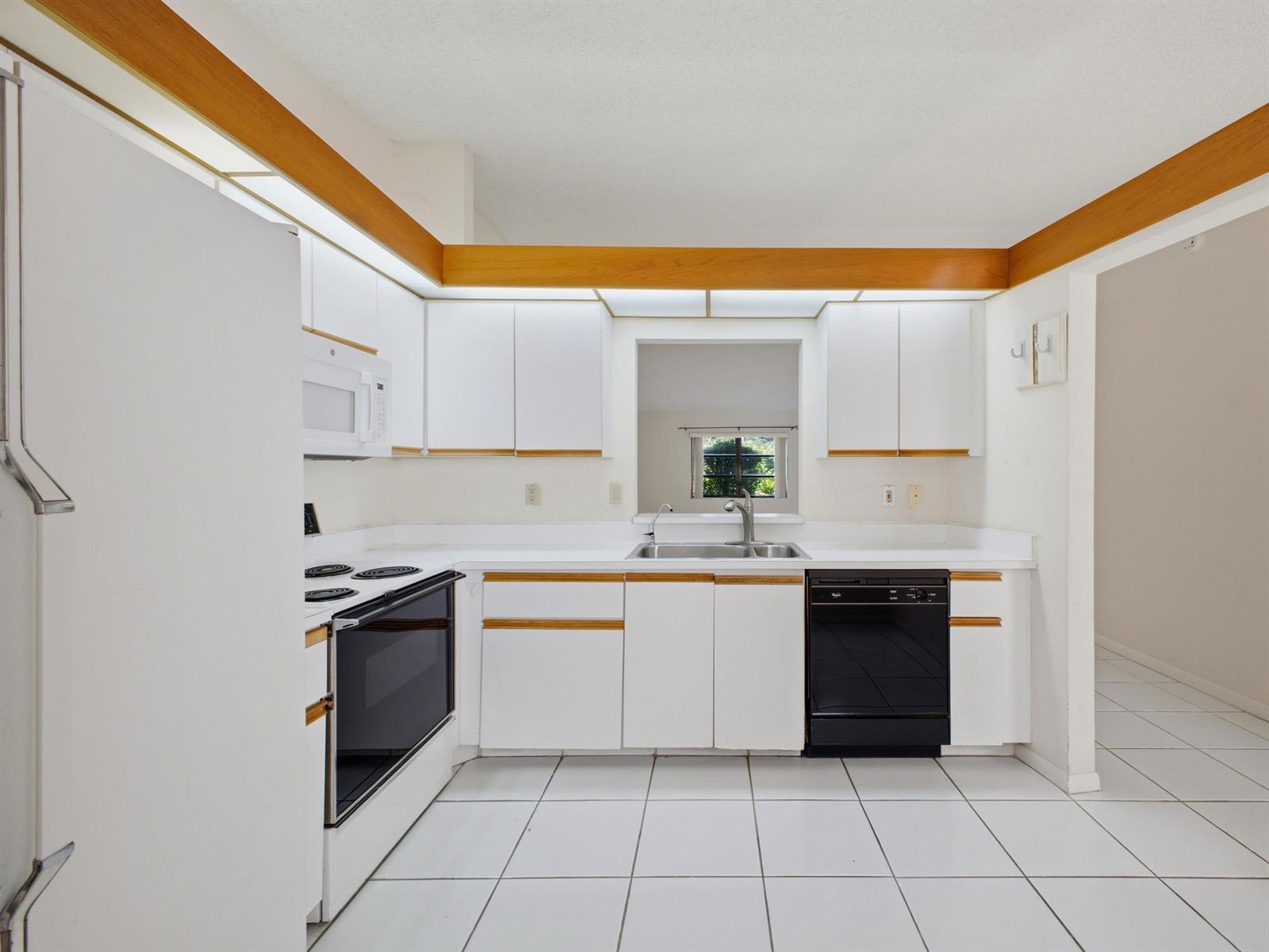 A kitchen with white cabinets, wood trim, white tile floors, and black appliances — 6200 Kings Gate Circle, Delray Beach FL 33484, DELRAY BEACH, FL