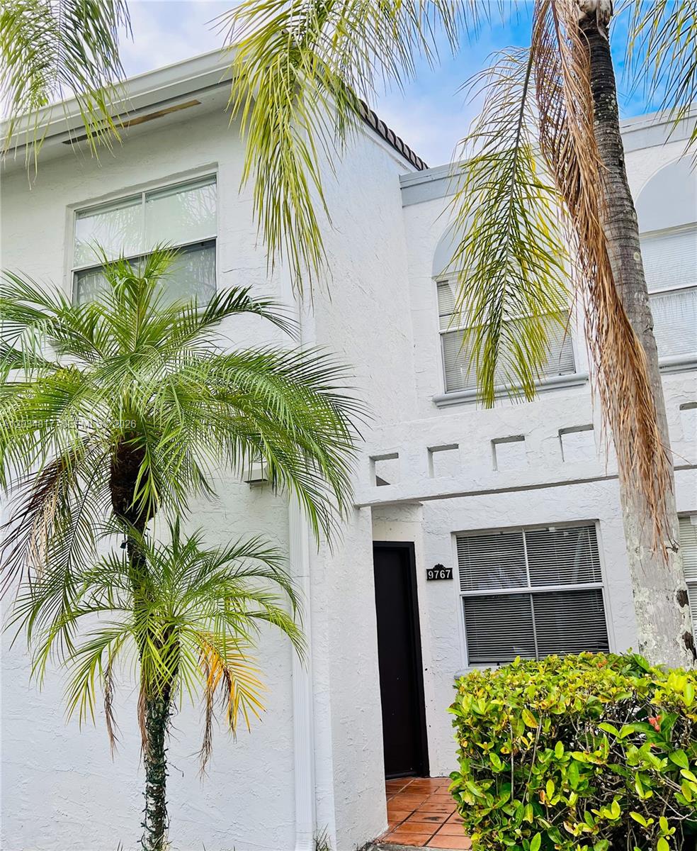 A two-story white stucco townhouse exterior features a palm tree and a front entrance — 9767 NW 46th Ter # 109, Doral FL 33178, DORAL, FL
