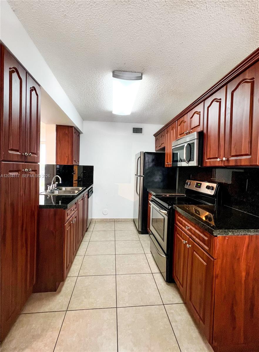A galley kitchen features dark wood cabinets, black countertops, and stainless steel appliances — 9767 NW 46th Ter # 109, Doral FL 33178, DORAL, FL
