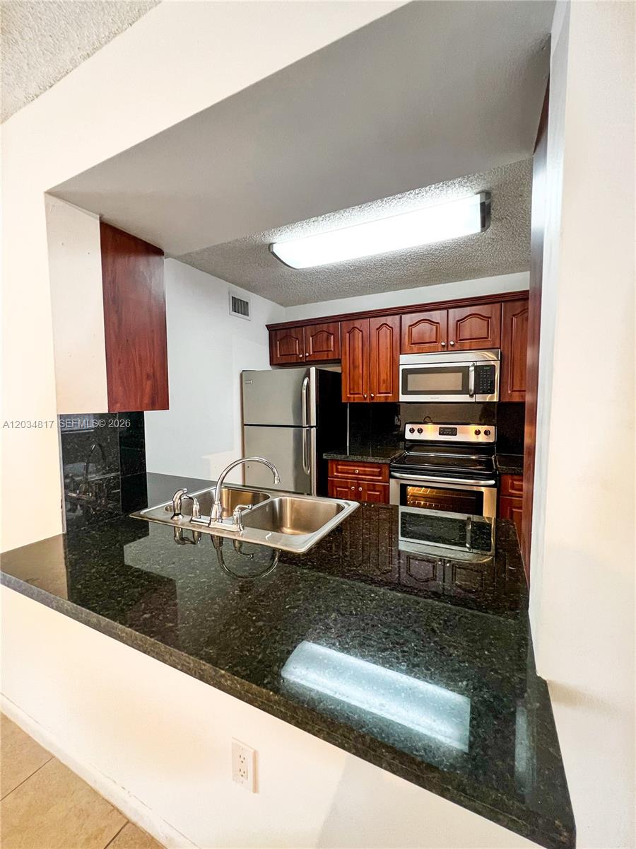 A kitchen features dark wood cabinets, black granite countertops, and stainless steel appliances — 9767 NW 46th Ter # 109, Doral FL 33178, DORAL, FL