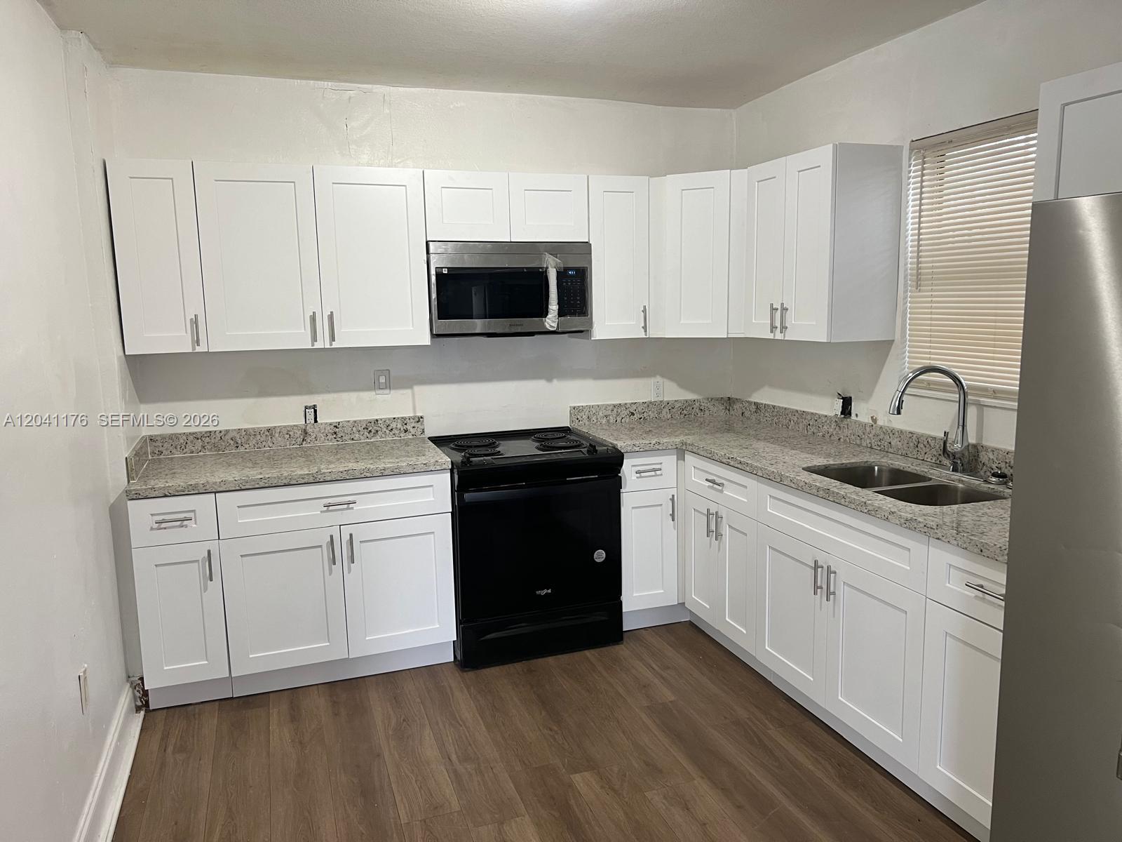 A kitchen features white shaker cabinets, granite countertops, and black appliances over wood-look flooring — 10 NW 71st St, Miami FL 33150, MIAMI, FL