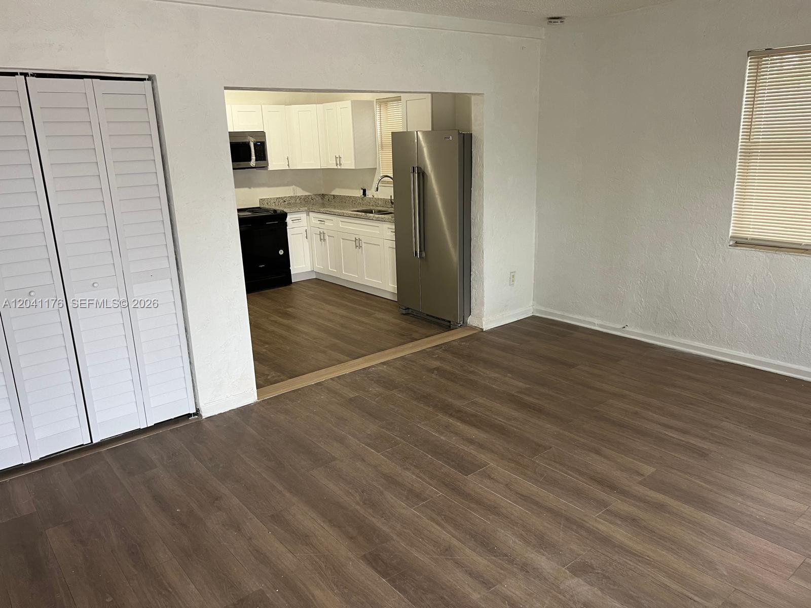 A living area with wood-look flooring leads into a kitchen featuring white cabinets and appliances — 10 NW 71st St, Miami FL 33150, MIAMI, FL