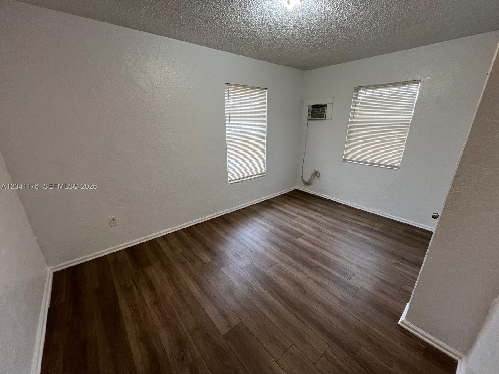 An empty bedroom features white walls, dark wood-look flooring, two windows, and a wall-mounted air conditioner — 10 NW 71st St, Miami FL 33150, MIAMI, FL