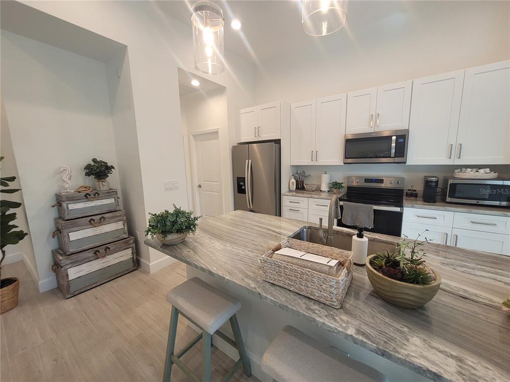 A kitchen features white cabinets, stainless steel appliances, and a stone-topped island with seating — 67 SUCCESS DRIVE, PUNTA GORDA, FL