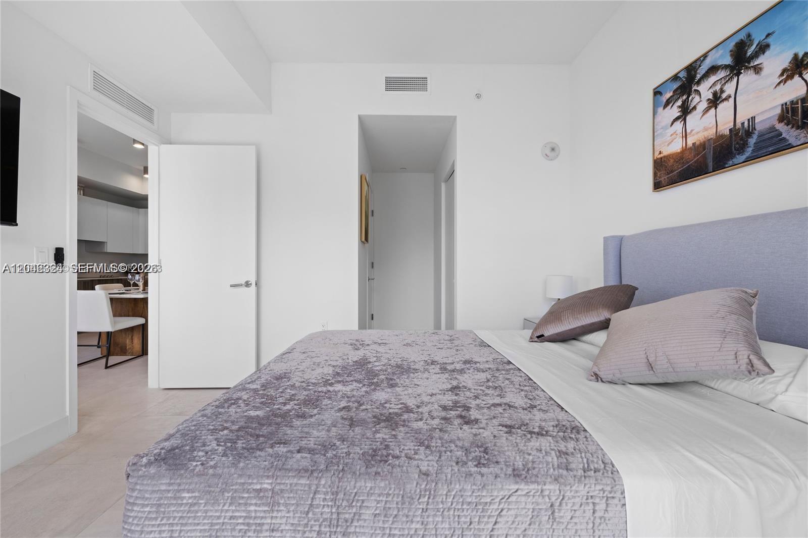 A bedroom features a gray upholstered bed, white walls, and a doorway leading to a kitchen — 239 SW 9th St # 1502, Miami FL 33130, MIAMI, FL