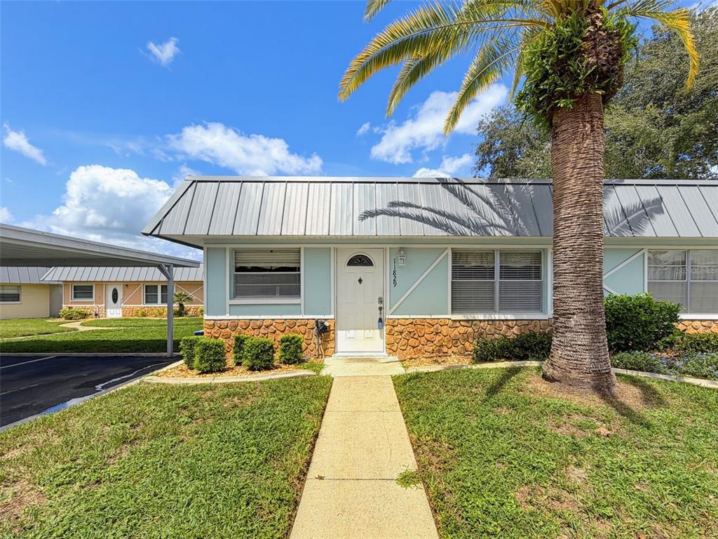 A single-story home with a metal roof, stone facade, and a palm tree in front — 11829 CARISSA LANE UNIT A, NEW PORT RICHEY, FL