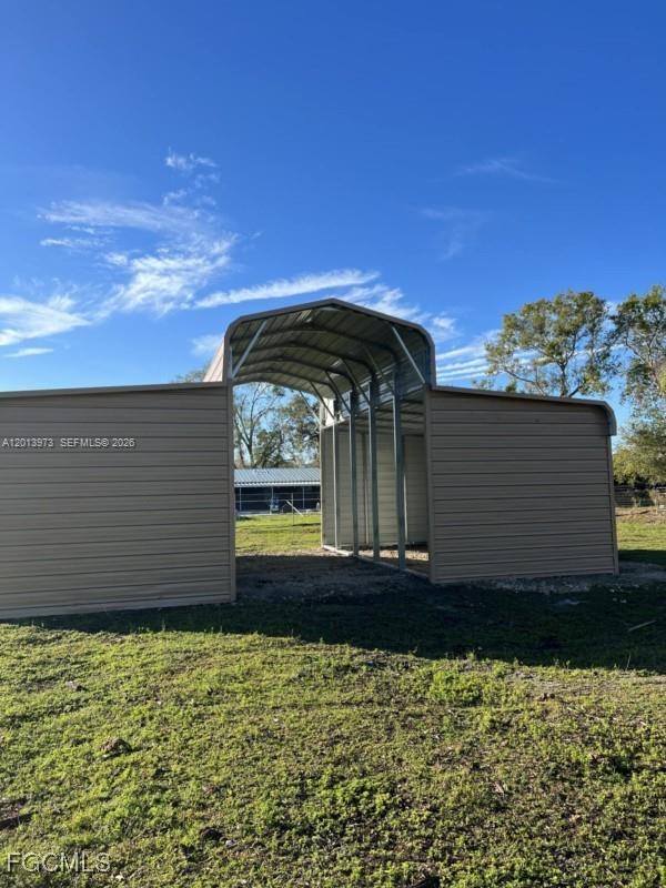 A metal carport structure with side walls stands on a grassy lot under blue skies — 826 B Rd., La Belle FL 33935, LA BELLE, FL