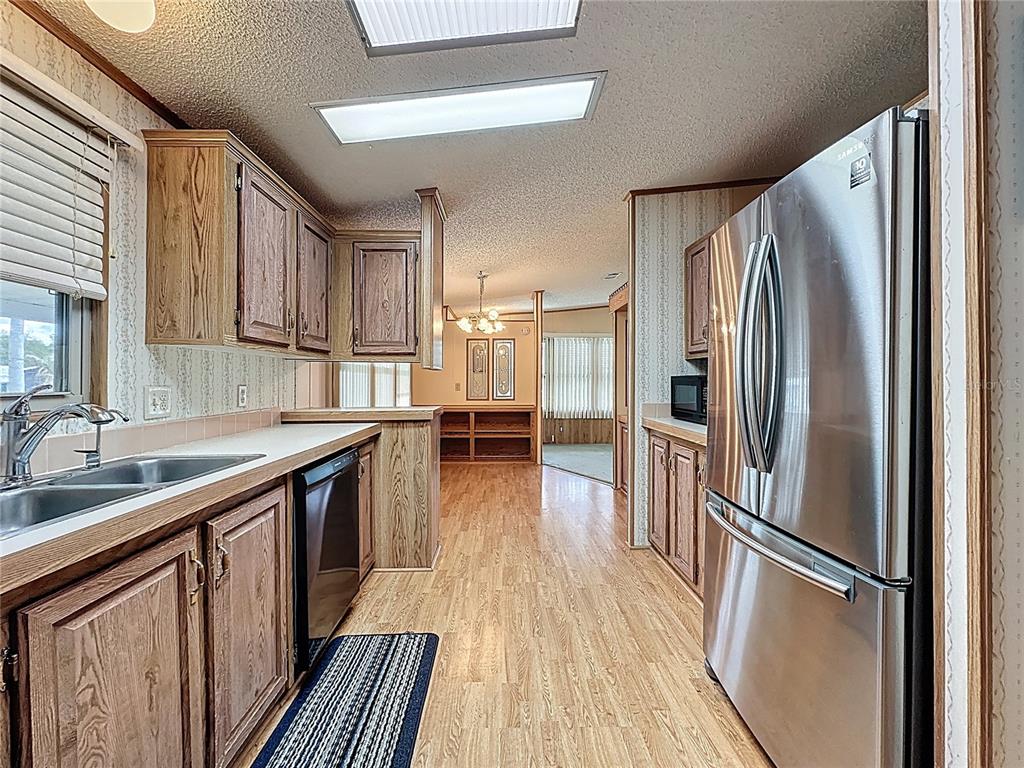 A kitchen with wood cabinets, stainless steel appliances, and laminate flooring leads to a dining area — 449 TIVOLI PARK DRIVE, DAVENPORT, FL