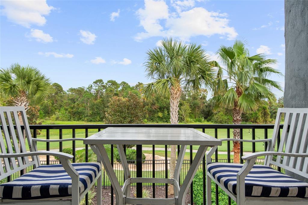 A balcony with a small table and two chairs overlooking palm trees and greenery — 945 DESERT MOUNTAIN COURT, REUNION, FL