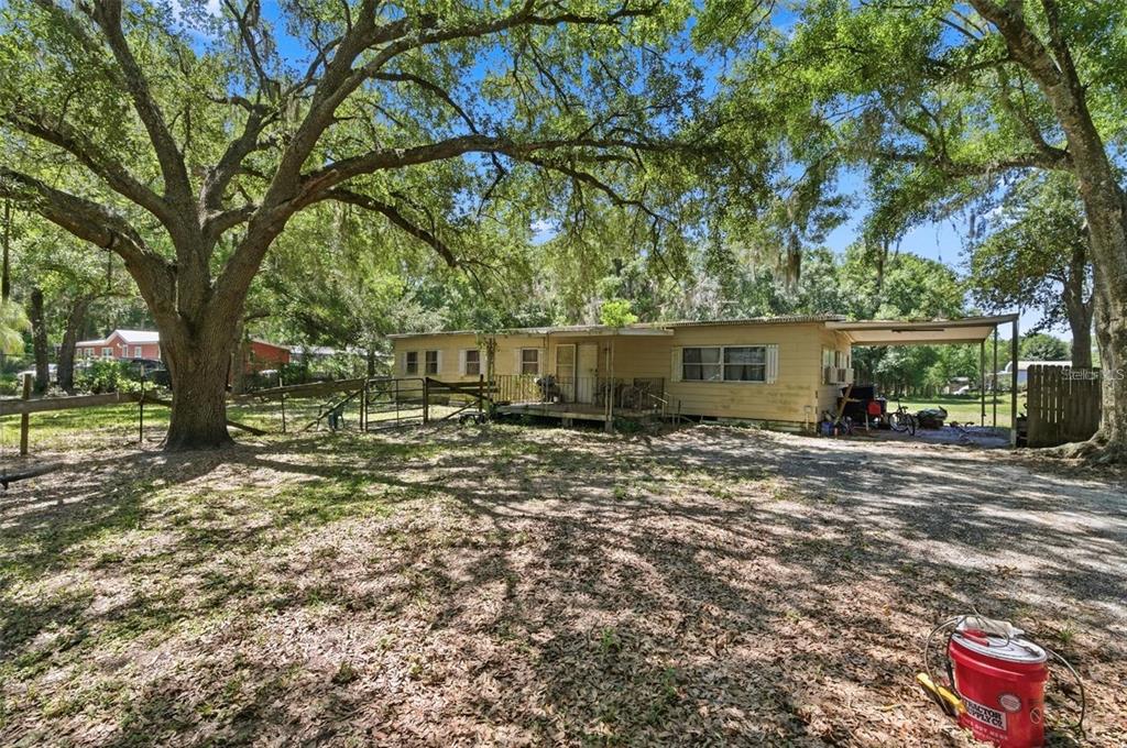 A single-story mobile home with a front porch sits on a dirt lot under trees — 17214 CHINABERRY ROAD, LUTZ, FL