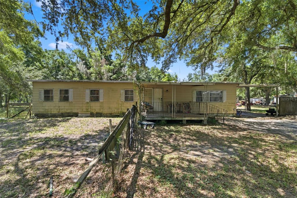 A single-story mobile home with a front porch sits on a wooded, fenced lot — 17214 CHINABERRY ROAD, LUTZ, FL