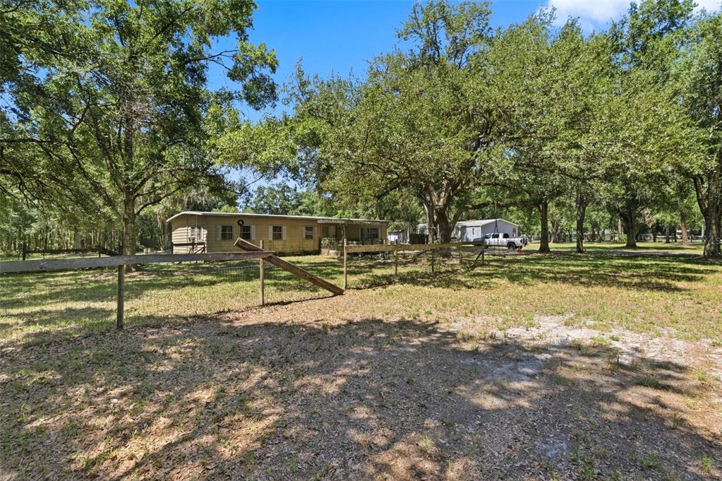 A single-story house sits behind a wooden fence on a large, tree-shaded grassy lot — 17214 CHINABERRY ROAD, LUTZ, FL