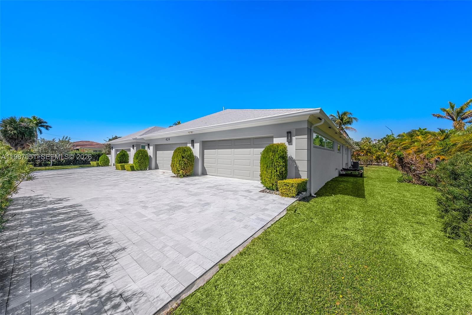 A gray house with a paved driveway and a large green lawn under a blue sky — 424 Alamanda Dr, Hallandale Beach FL 33009, HALLANDALE BEACH, FL