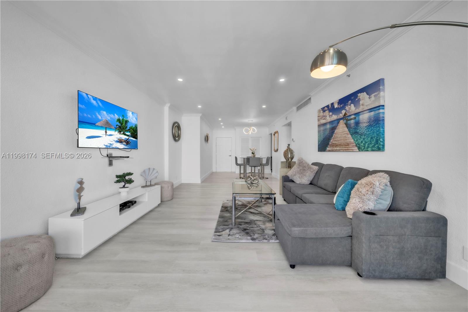 A living room with light wood floors, a grey sectional sofa, and a wall-mounted television — 2501 S Ocean Dr, Hollywood FL 33019, HOLLYWOOD, FL