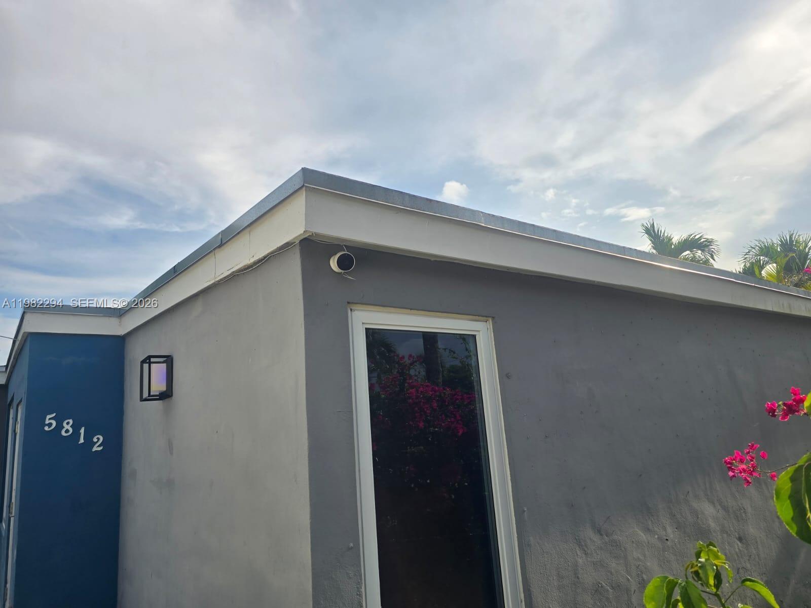 The exterior of a gray building features a blue accent wall, house numbers, and a camera — 5812 NW 20th Ct, Margate FL 33063, MARGATE, FL