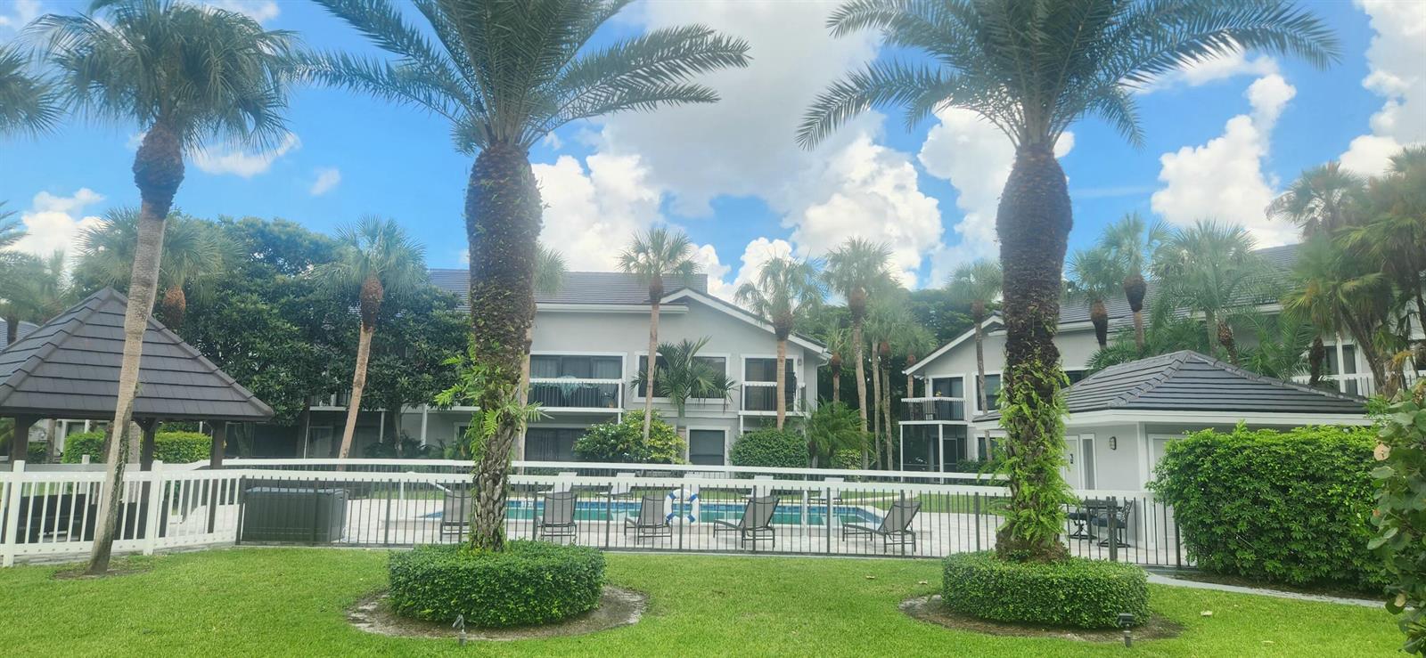 A swimming pool is enclosed by a fence in front of a two-story apartment building — 11863 Wimbledon Circle # 416, Wellington FL 33414, WELLINGTON, FL