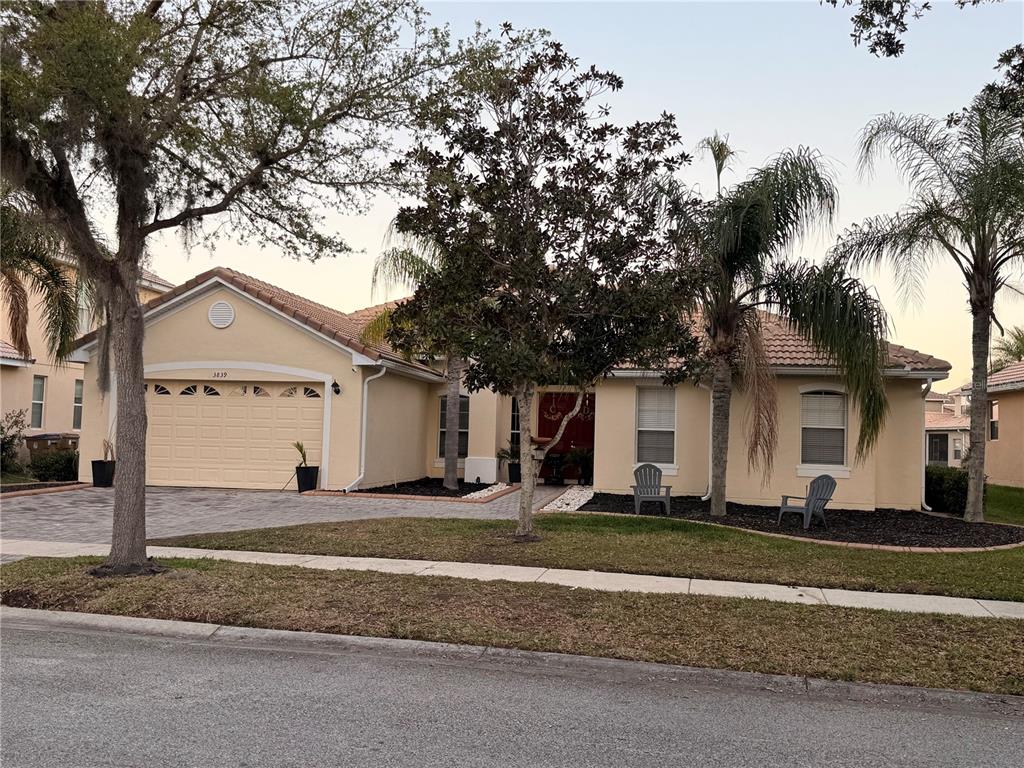 A single-story tan house with a two-car garage, tile roof, and front yard landscaping — 3839 GOLDEN FEATHER WAY, KISSIMMEE, FL