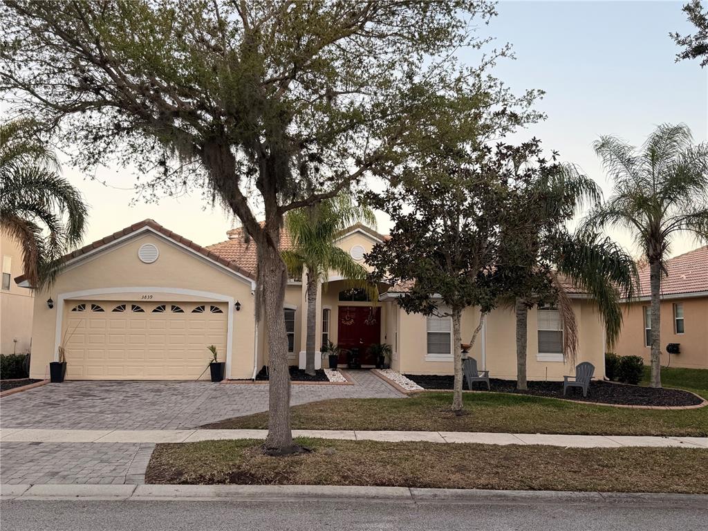 A single-story house with a beige stucco exterior, a two-car garage, and a paved driveway — 3839 GOLDEN FEATHER WAY, KISSIMMEE, FL