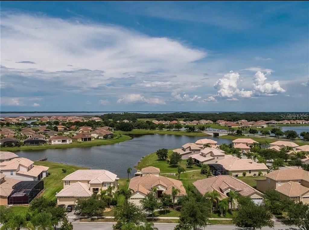 An aerial view of a suburban neighborhood featuring houses surrounding a lake under a cloudy sky — 3839 GOLDEN FEATHER WAY, KISSIMMEE, FL