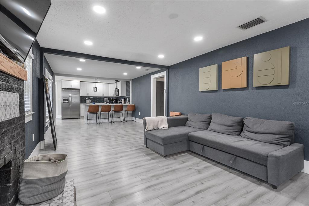 A living room with gray flooring and a sectional sofa opens into a kitchen area — 806 E HAMILTON AVENUE, TAMPA, FL