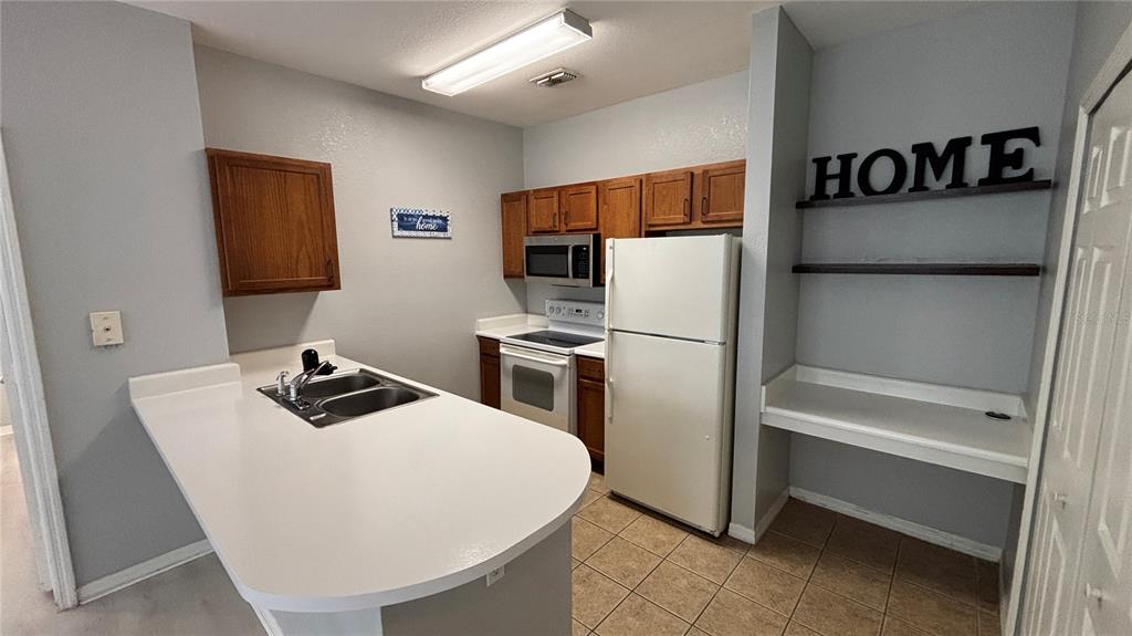 A kitchen features light gray walls, wooden cabinets, white appliances, and a peninsula sink — 8103 LILLIES WAY UNIT 108, ORLANDO, FL