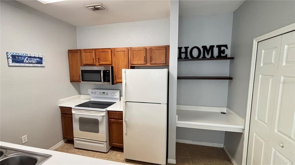 A kitchen features wood cabinets, white appliances, and a built-in desk area with shelves — 8103 LILLIES WAY UNIT 108, ORLANDO, FL