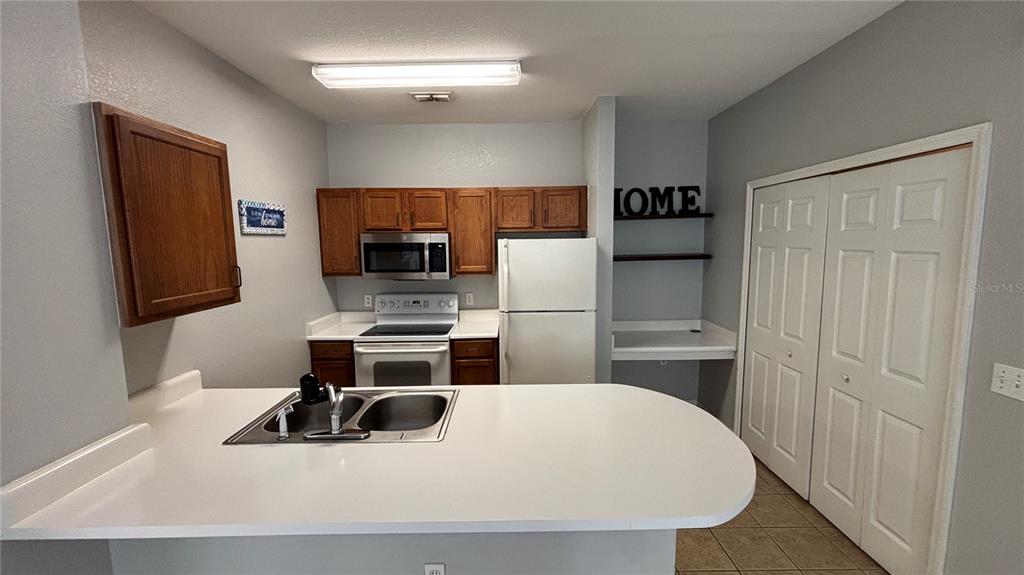 A kitchen features white countertops, wooden cabinets, a white refrigerator, and a double-door closet — 8103 LILLIES WAY UNIT 108, ORLANDO, FL