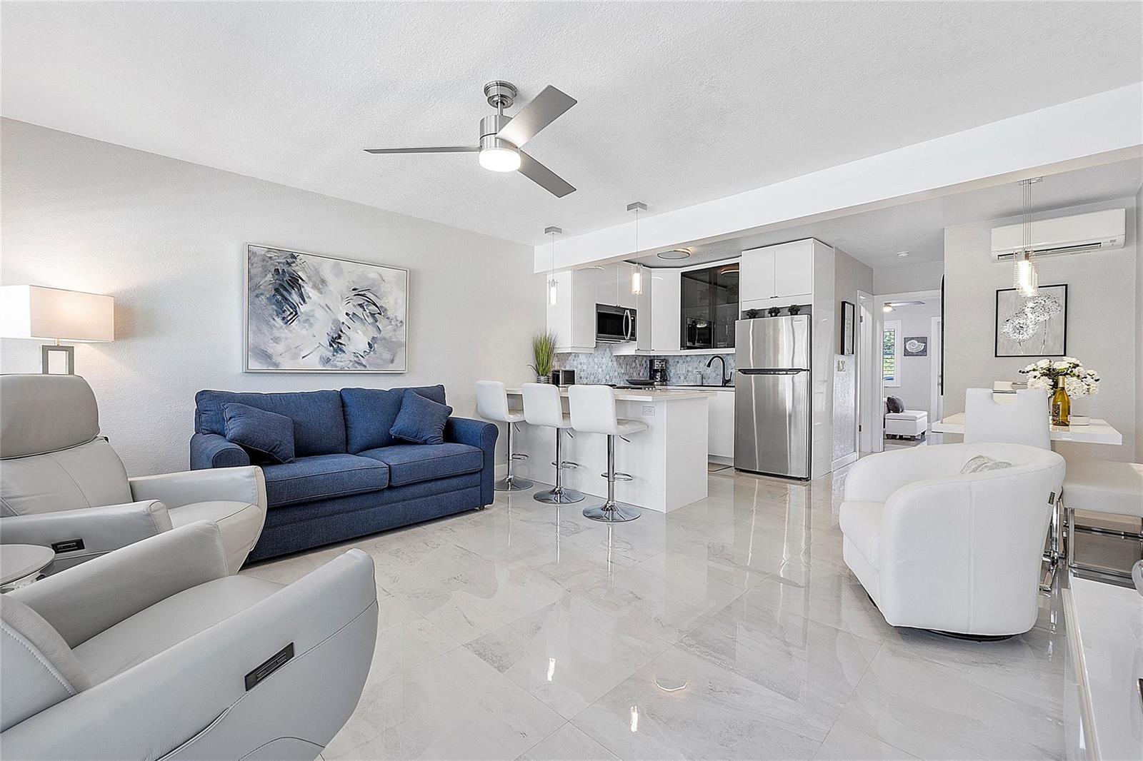 An open-concept living area features a blue sofa, white armchairs, and a modern kitchen — 500 Layne Boulevard # 6, Hallandale Beach FL 33009, HALLANDALE BEACH, FL
