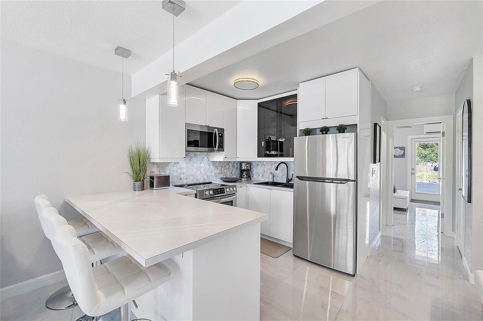A modern kitchen features white cabinets, stainless steel appliances, a breakfast bar, and tiled floors — 500 Layne Boulevard # 6, Hallandale Beach FL 33009, HALLANDALE BEACH, FL