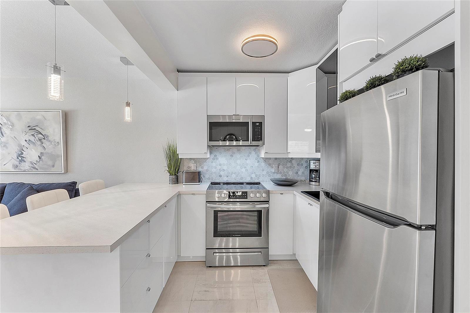 A modern kitchen features white glossy cabinets, stainless steel appliances, and a light-colored countertop — 500 Layne Boulevard # 6, Hallandale Beach FL 33009, HALLANDALE BEACH, FL