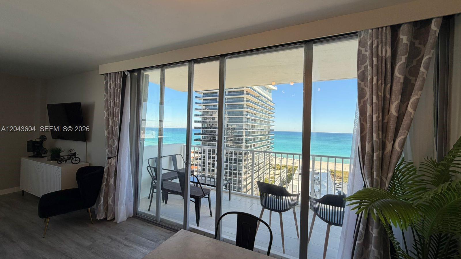 A living room with a balcony overlooking the ocean and a neighboring high-rise building — 5838 Collins Ave # 15H, Miami Beach FL 33140, MIAMI BEACH, FL