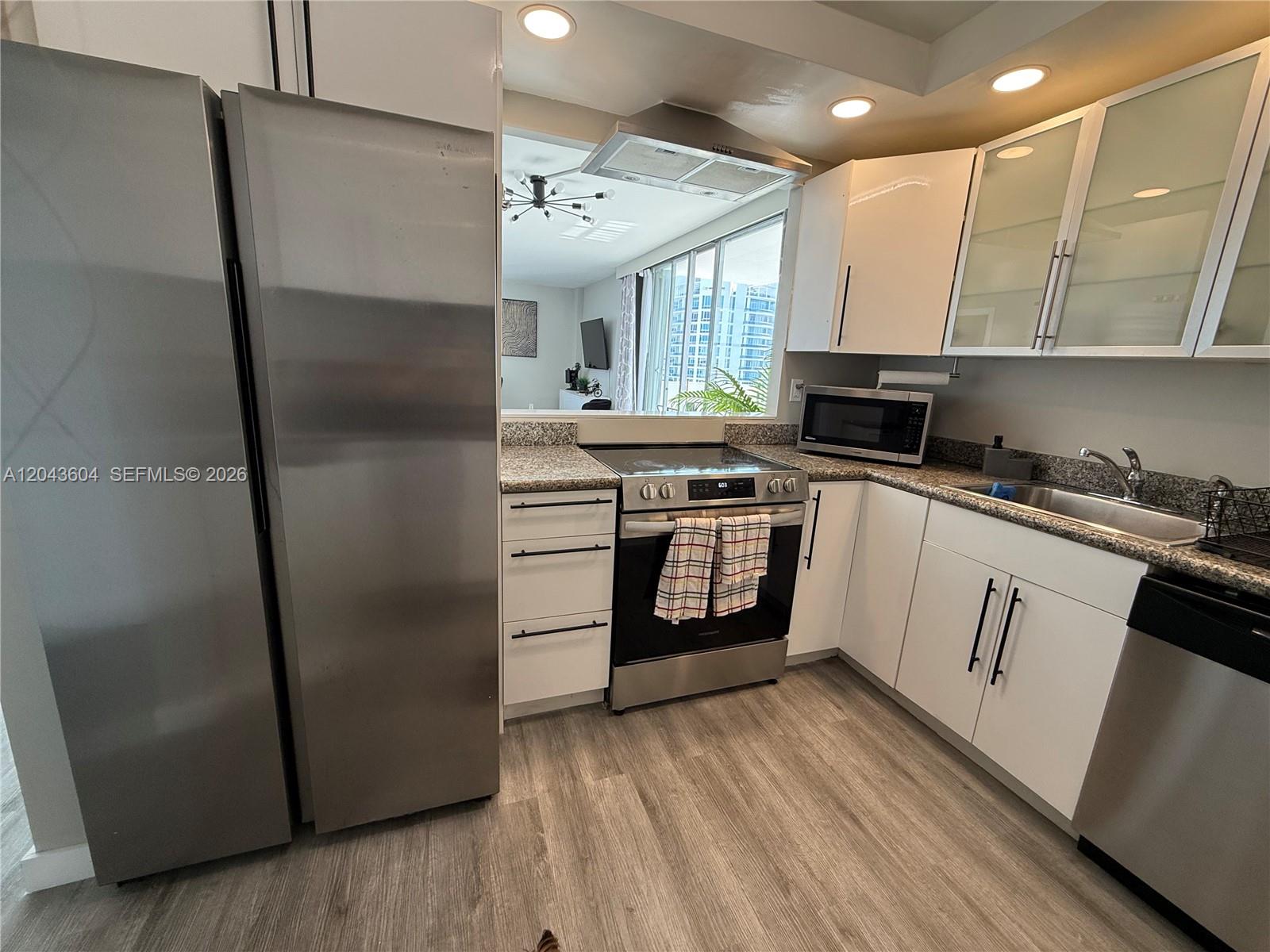 A kitchen features stainless steel appliances, white cabinetry, and a pass-through window to the living area — 5838 Collins Ave # 15H, Miami Beach FL 33140, MIAMI BEACH, FL
