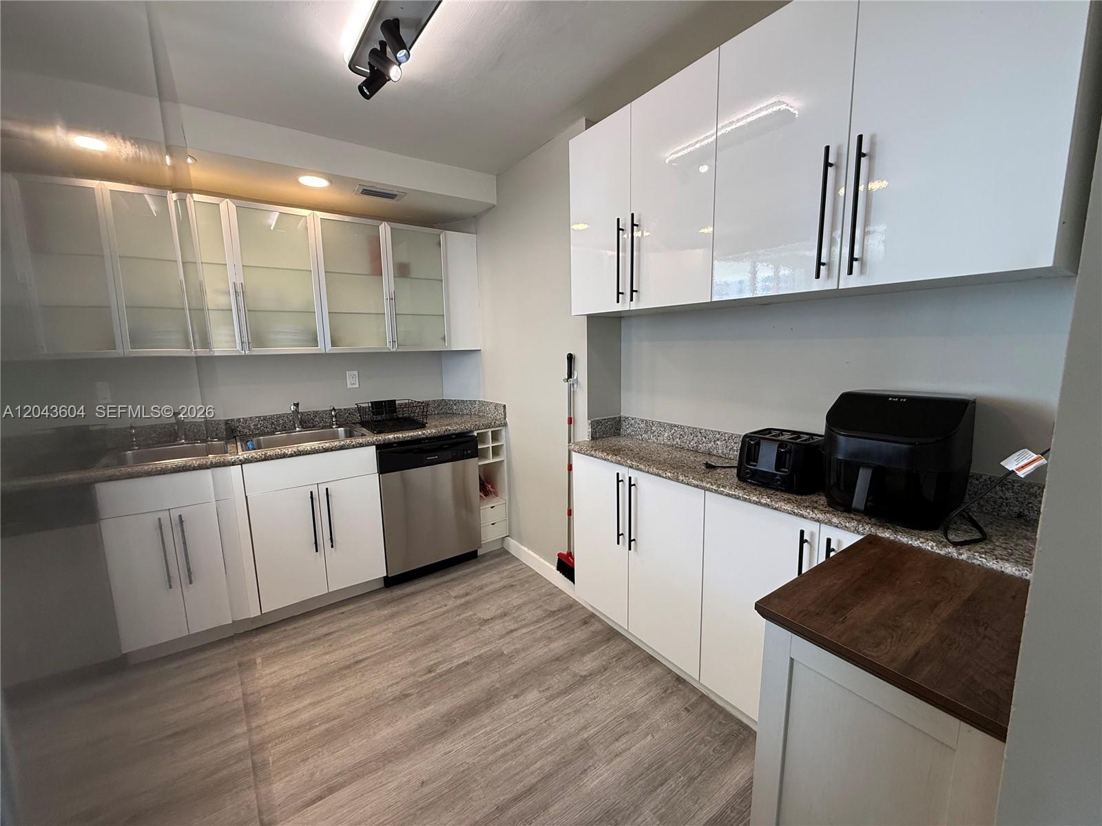 A kitchen features white cabinets, granite countertops, stainless steel appliances, and light wood-look flooring — 5838 Collins Ave # 15H, Miami Beach FL 33140, MIAMI BEACH, FL