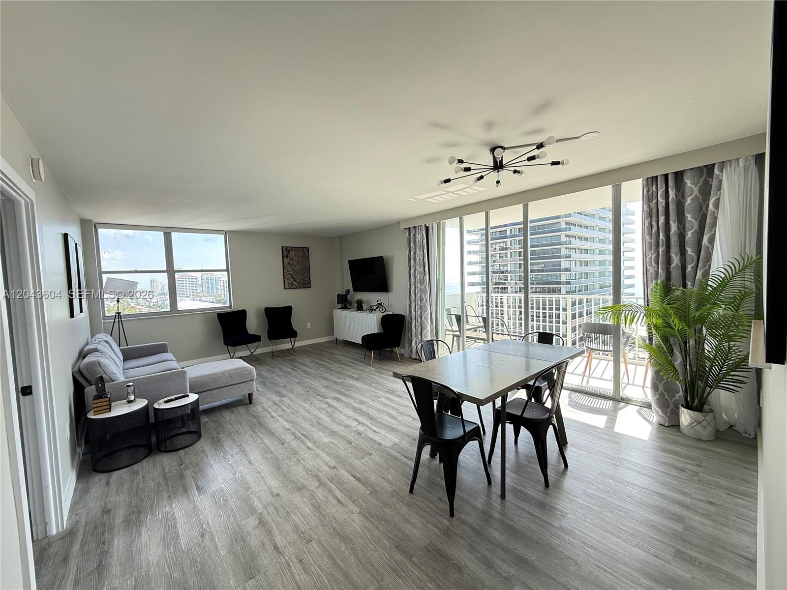 A bright living and dining area features light wood floors, modern furniture, and balcony views — 5838 Collins Ave # 15H, Miami Beach FL 33140, MIAMI BEACH, FL
