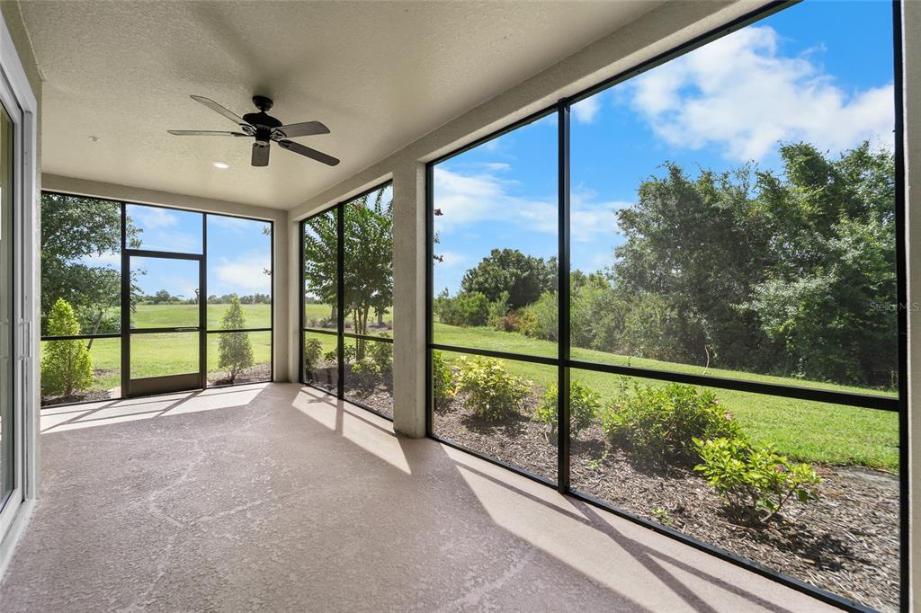 A screened-in patio with a ceiling fan overlooks a grassy yard and trees — 7342 DIVOT LOOP UNIT 1, LAKEWOOD RANCH, FL