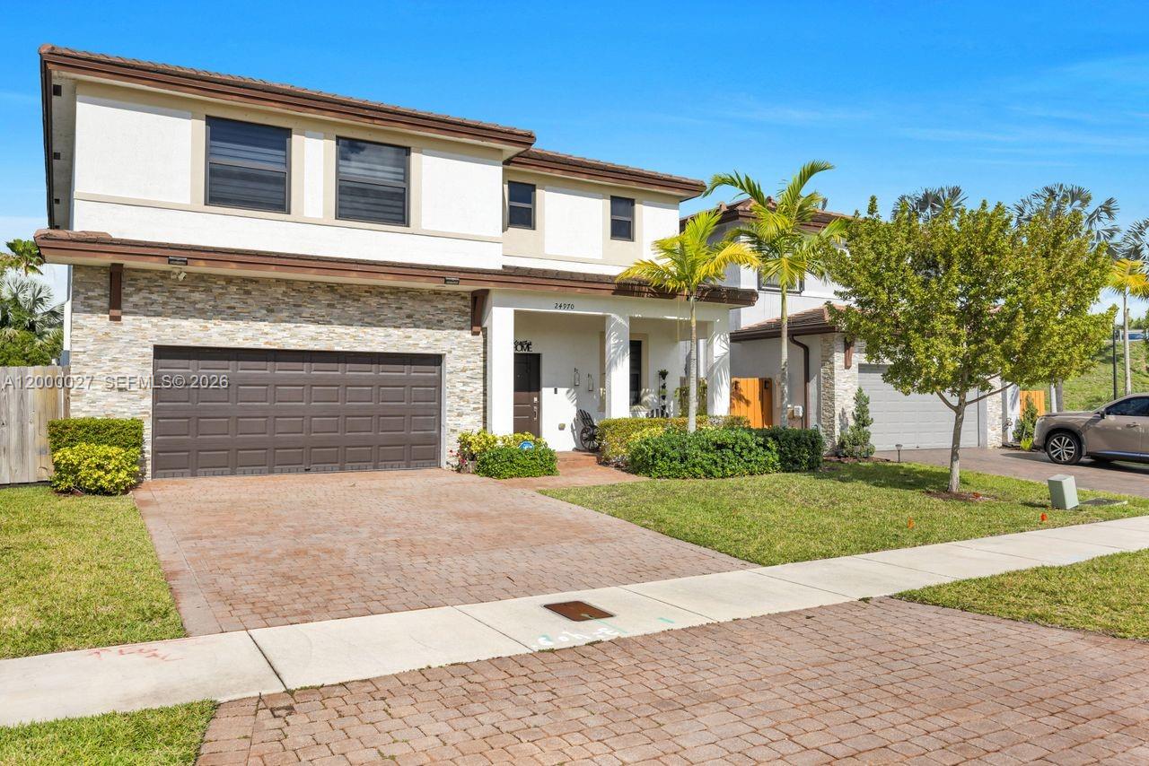 A two-story house features a stone facade, a brown garage door, and a paved driveway — 24970 SW 108th Ave, Homestead FL 33032, HOMESTEAD, FL