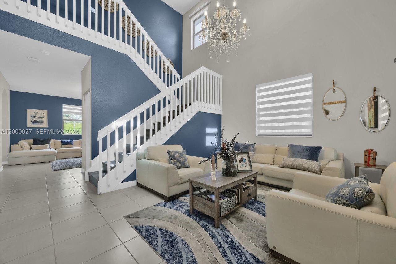 A living room features a white staircase, blue accent wall, chandelier, and light-colored furniture — 24970 SW 108th Ave, Homestead FL 33032, HOMESTEAD, FL