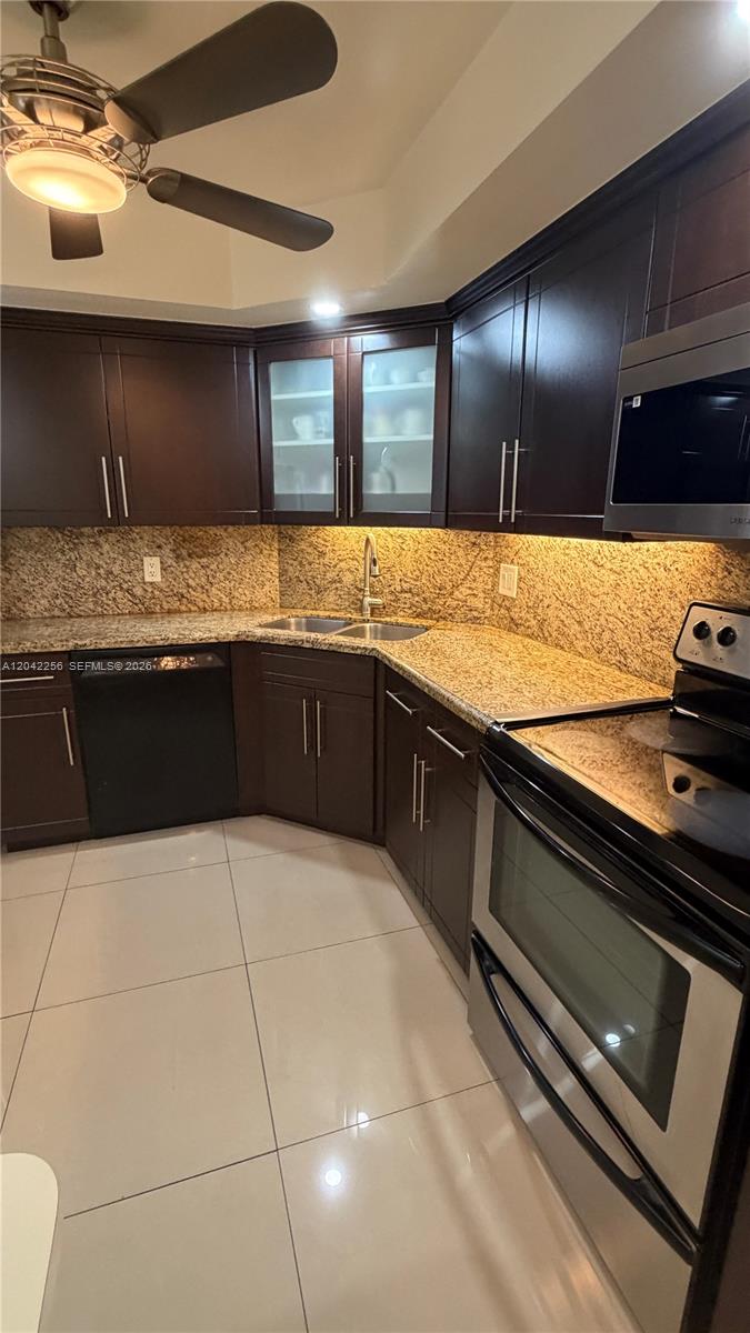 A kitchen features dark wood cabinets, granite countertops, stainless steel appliances, and tile flooring — 3280 Spanish Moss Ter # 214, Lauderhill FL 33319, LAUDERHILL, FL